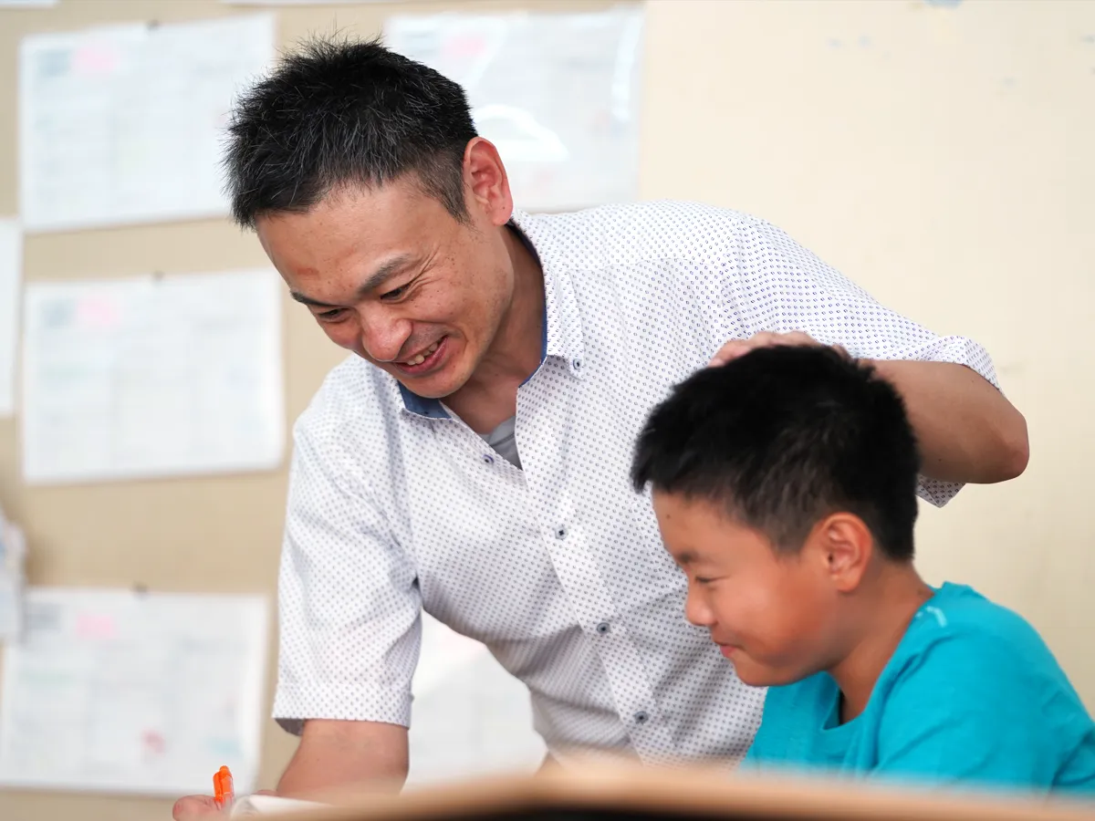 机に向かう児童の横で優しく指導する上山先生